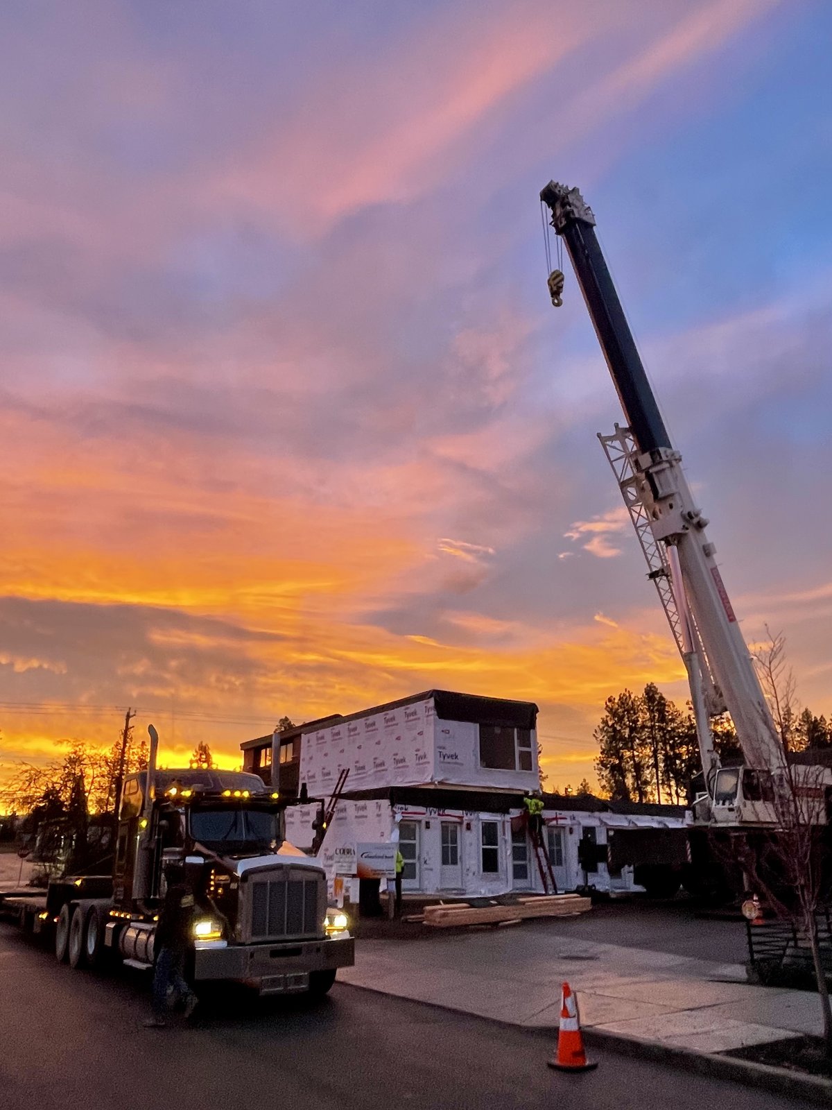 A crane and flatbed truck moving a modular building unit at sunset on a DanReDev project