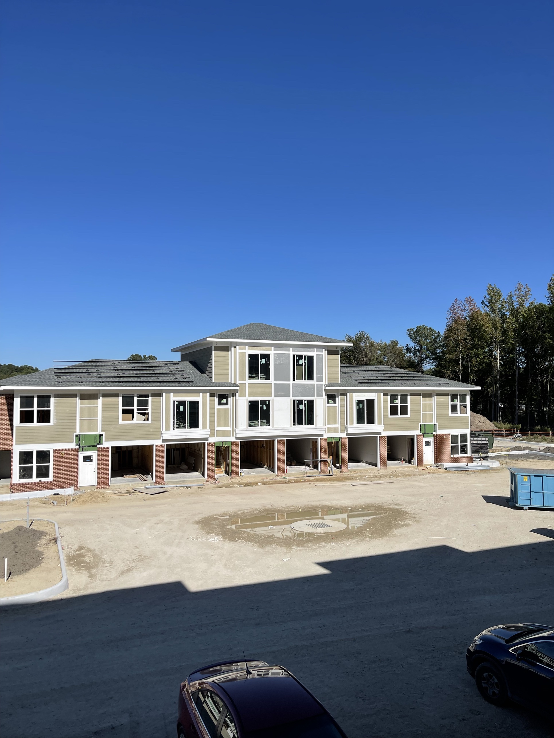 Brick-and-siding DanReDev townhomes nearing completion, roofs shingled and siding wrapped, with silt fencing still up to protect the site through final grading