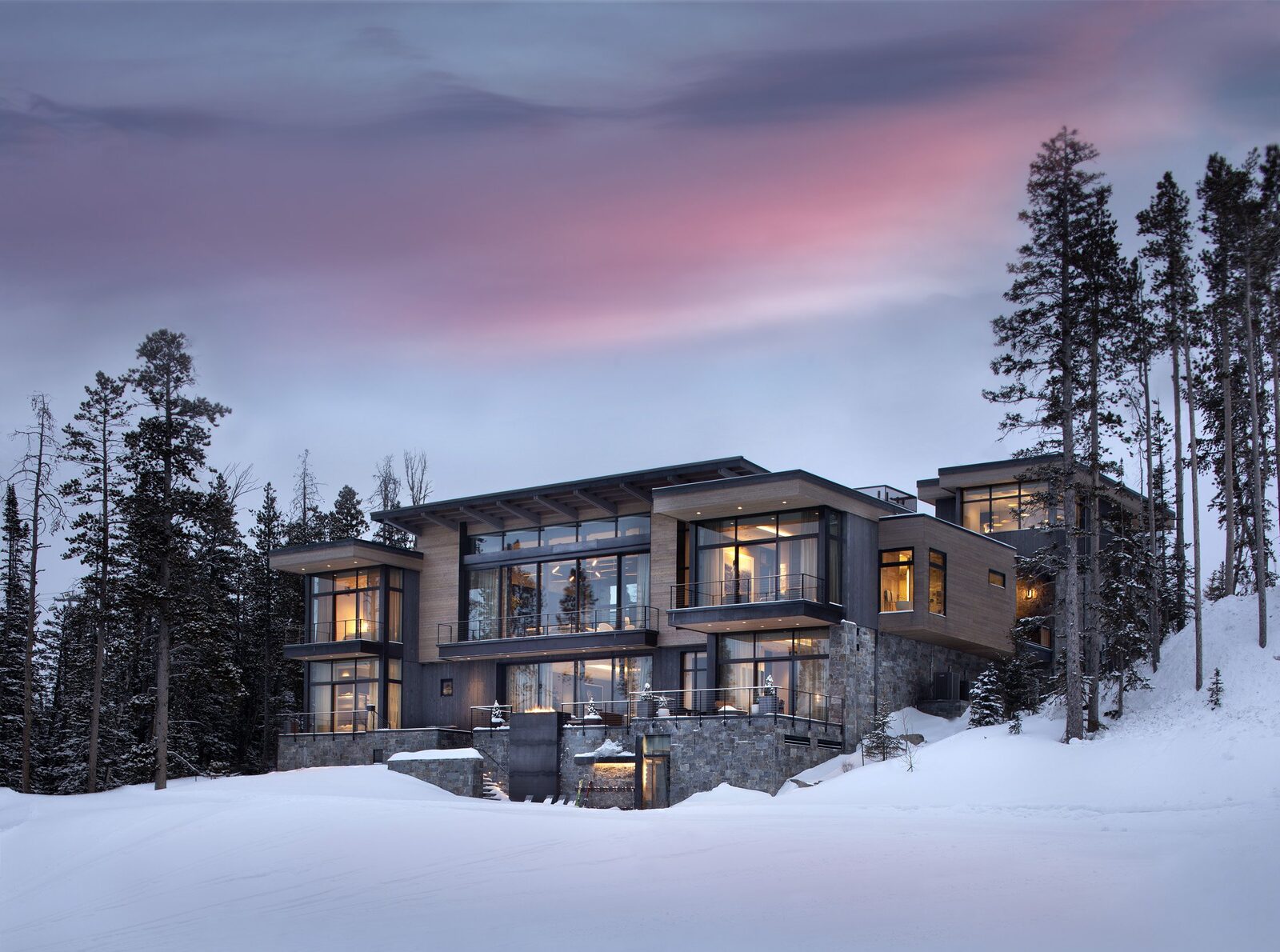 A modern DEK Builds mountain home at dusk in the snow