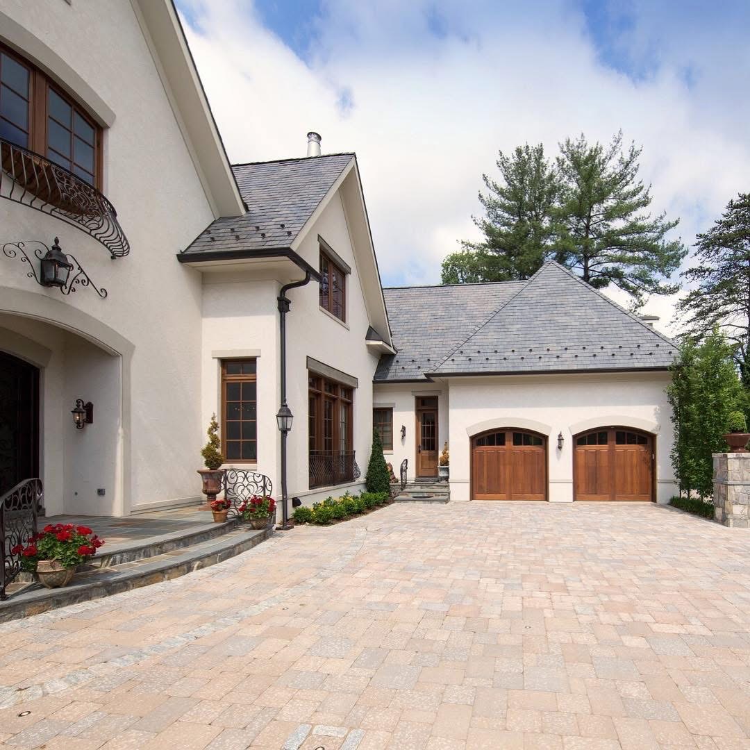 A DK Homes French-country style residence with arched wood garage doors and a stone driveway