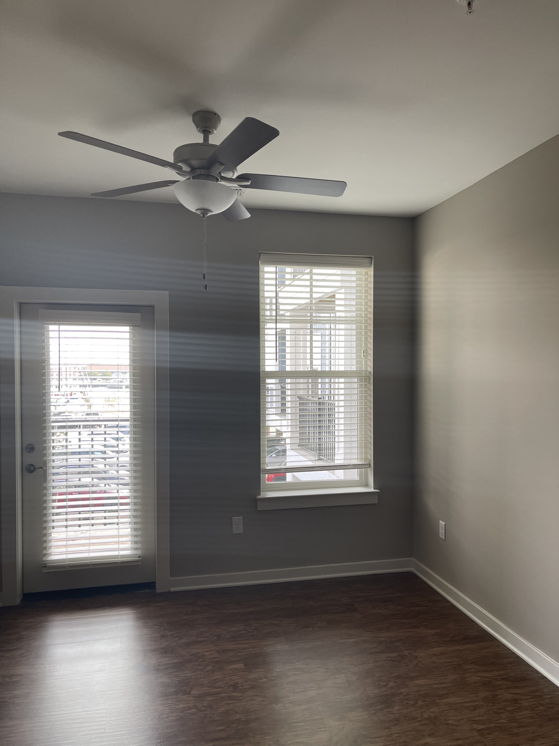 A bedroom with a ceiling fan, a glass patio door, and a tall window overlooking the parking area