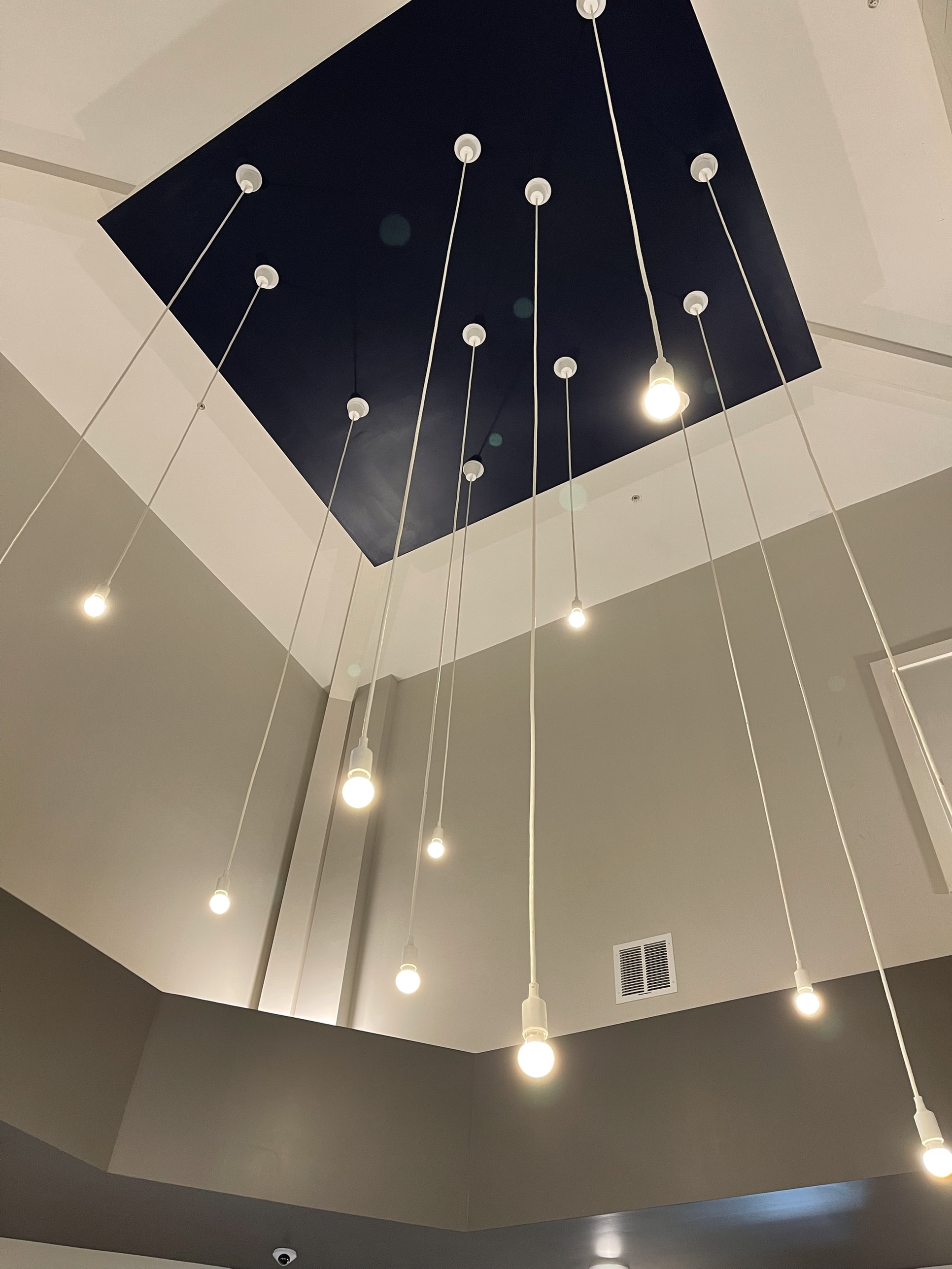 A cluster of pendant lights hanging from the two-story clubhouse foyer ceiling