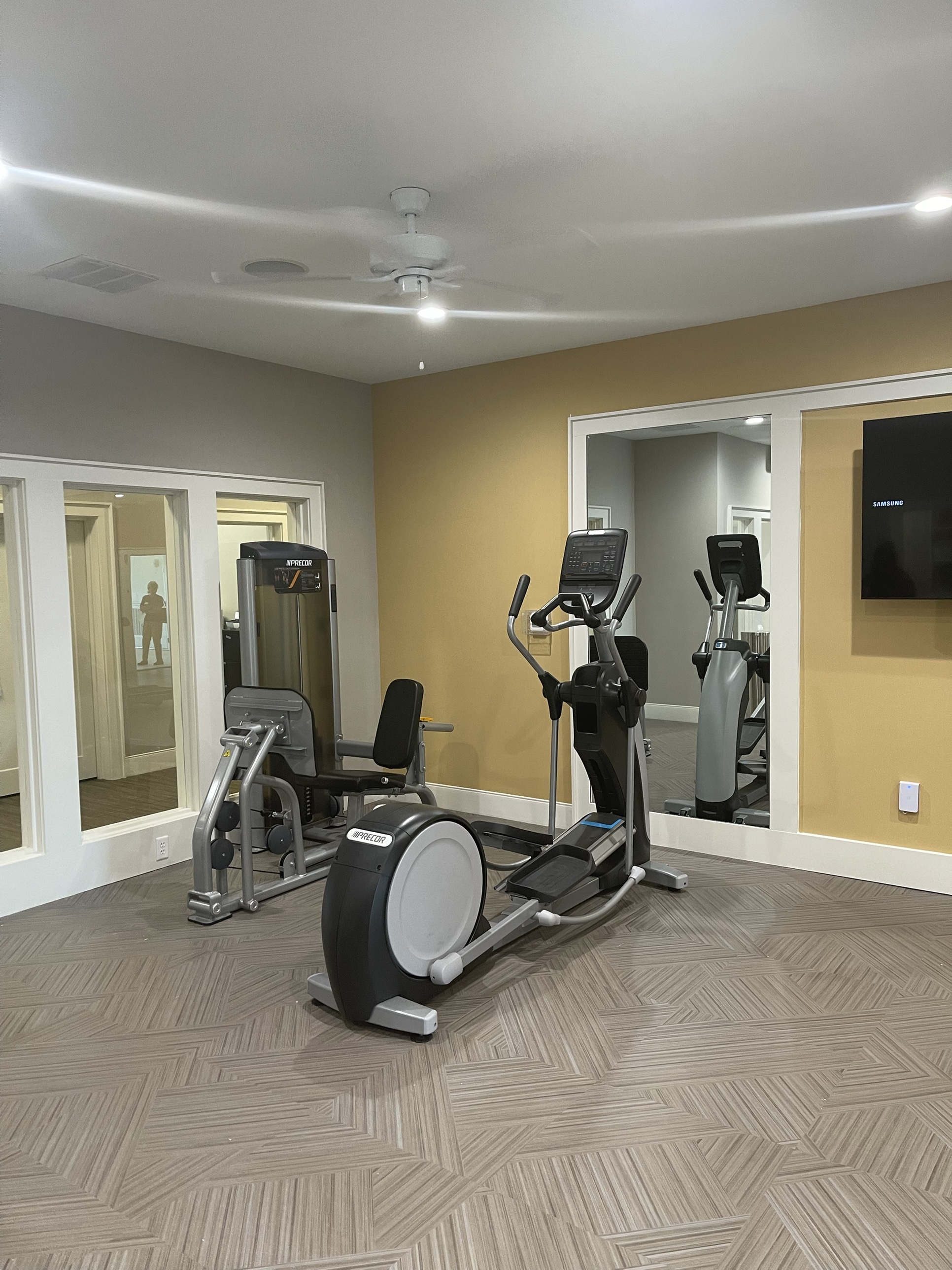 The resident fitness center with elliptical and leg press machines, mirrored walls, and a wall-mounted TV