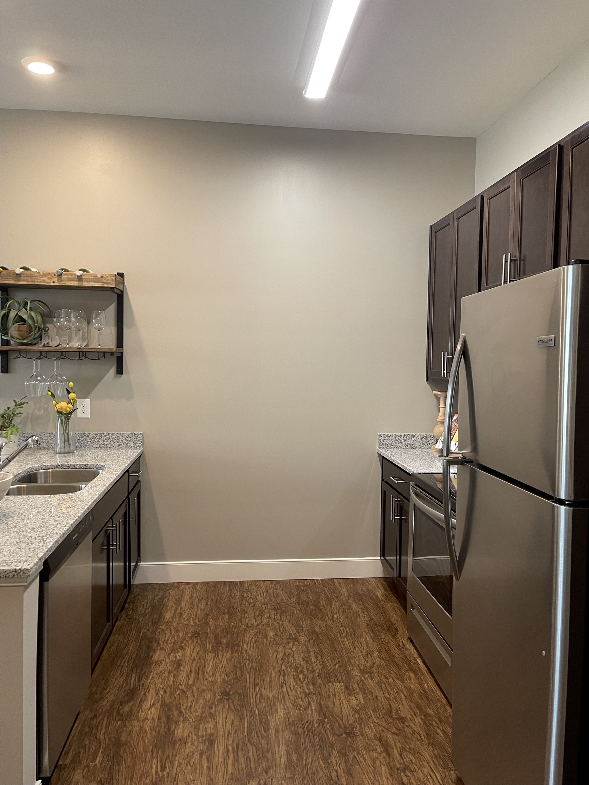 A finished galley kitchen with dark cabinetry, granite countertops, and a stainless steel refrigerator, range, and dishwasher