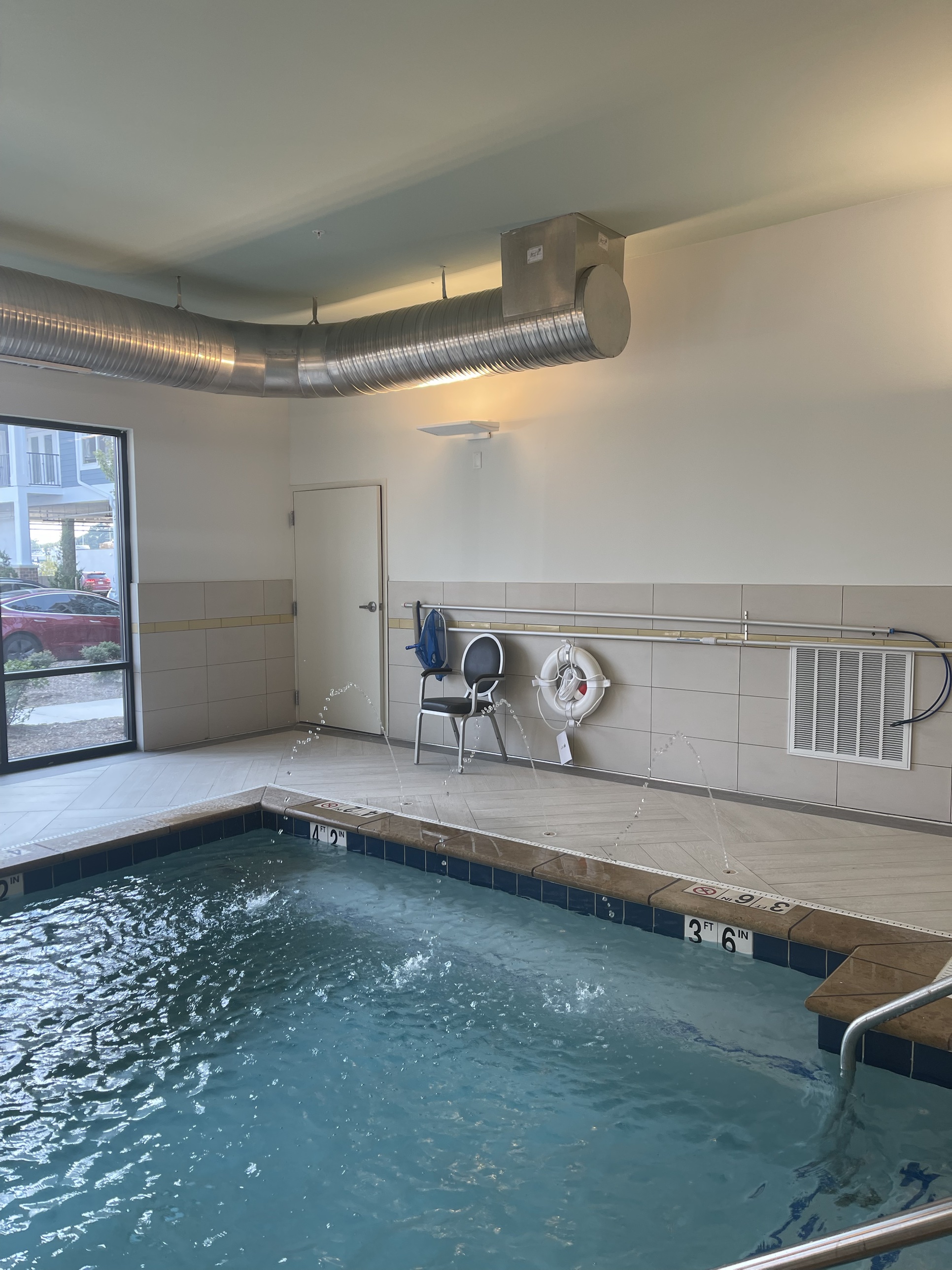 An indoor therapy pool with a tile surround, safety railing, and life ring