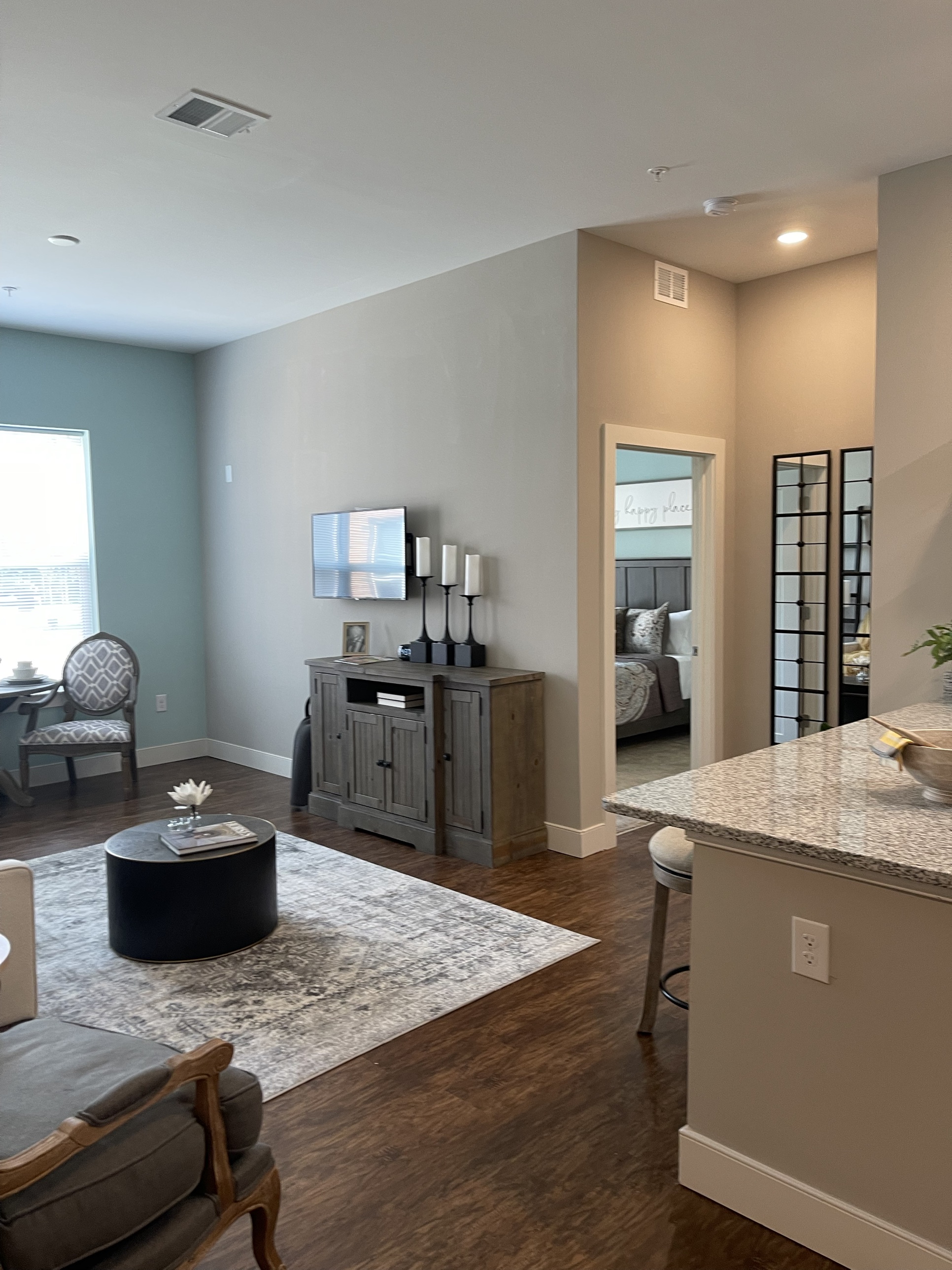 A furnished Greenview Residences living area with a teal accent wall, media console, and a view through to the kitchen island and a bedroom