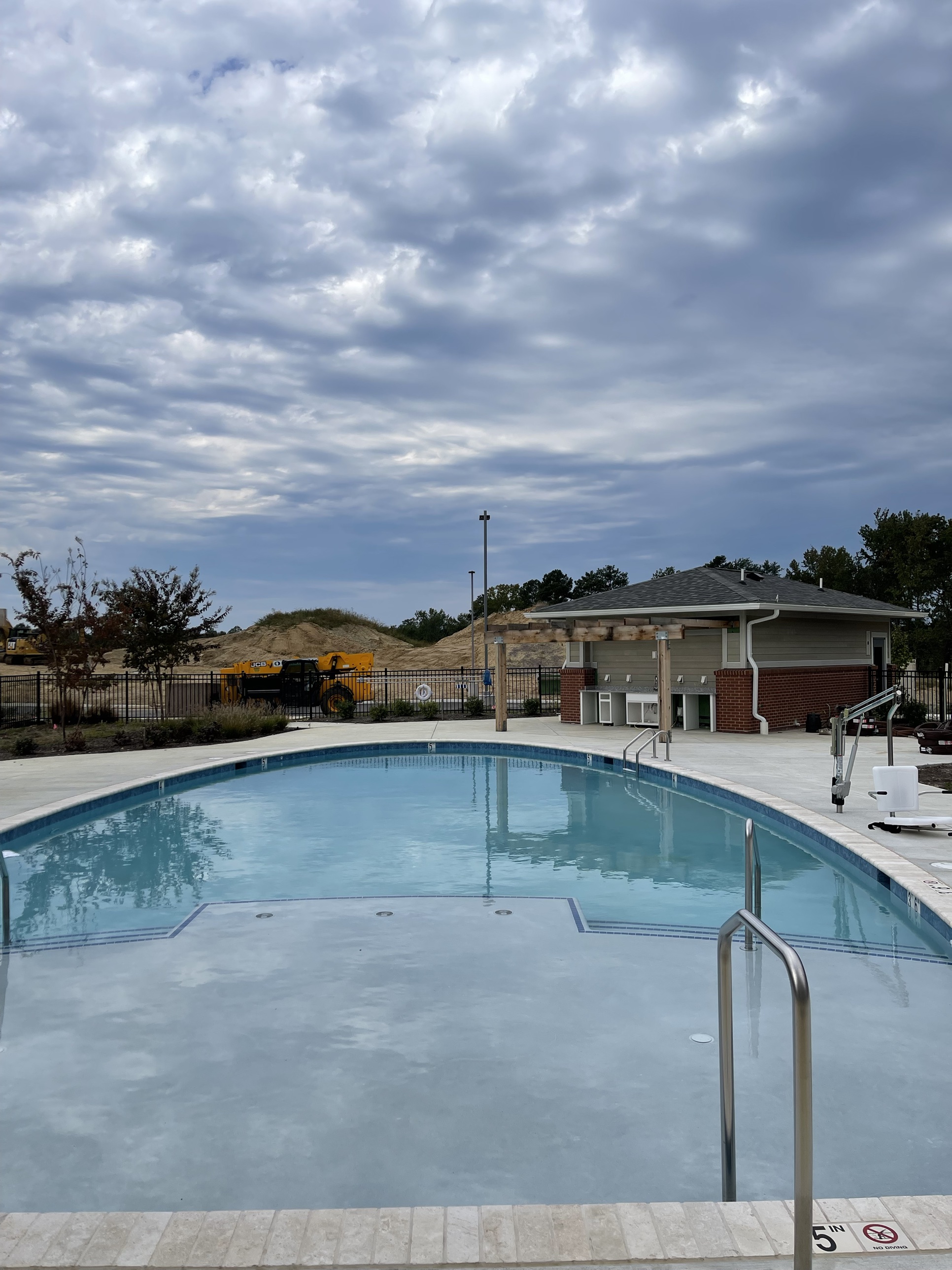 The Greenview Residences outdoor pool nearing completion, with grading equipment and a dirt stockpile still visible beyond the fence