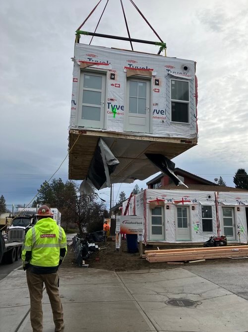 A crane lifting a Tyvek-wrapped Oldivai Project Zero module into place on site