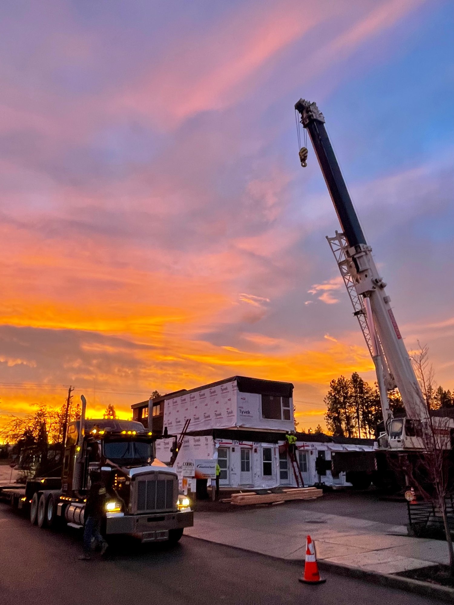 A crane and flatbed truck delivering an Oldivai Project Zero module to the Spokane site at sunset