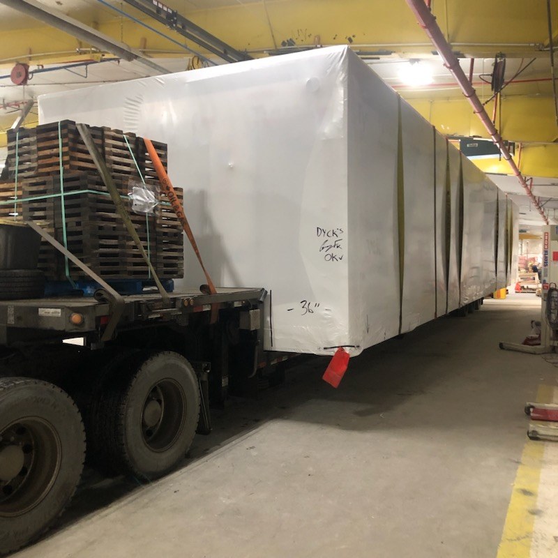 A shrink-wrapped Oldivai Project Zero module loaded on a flatbed trailer inside the factory