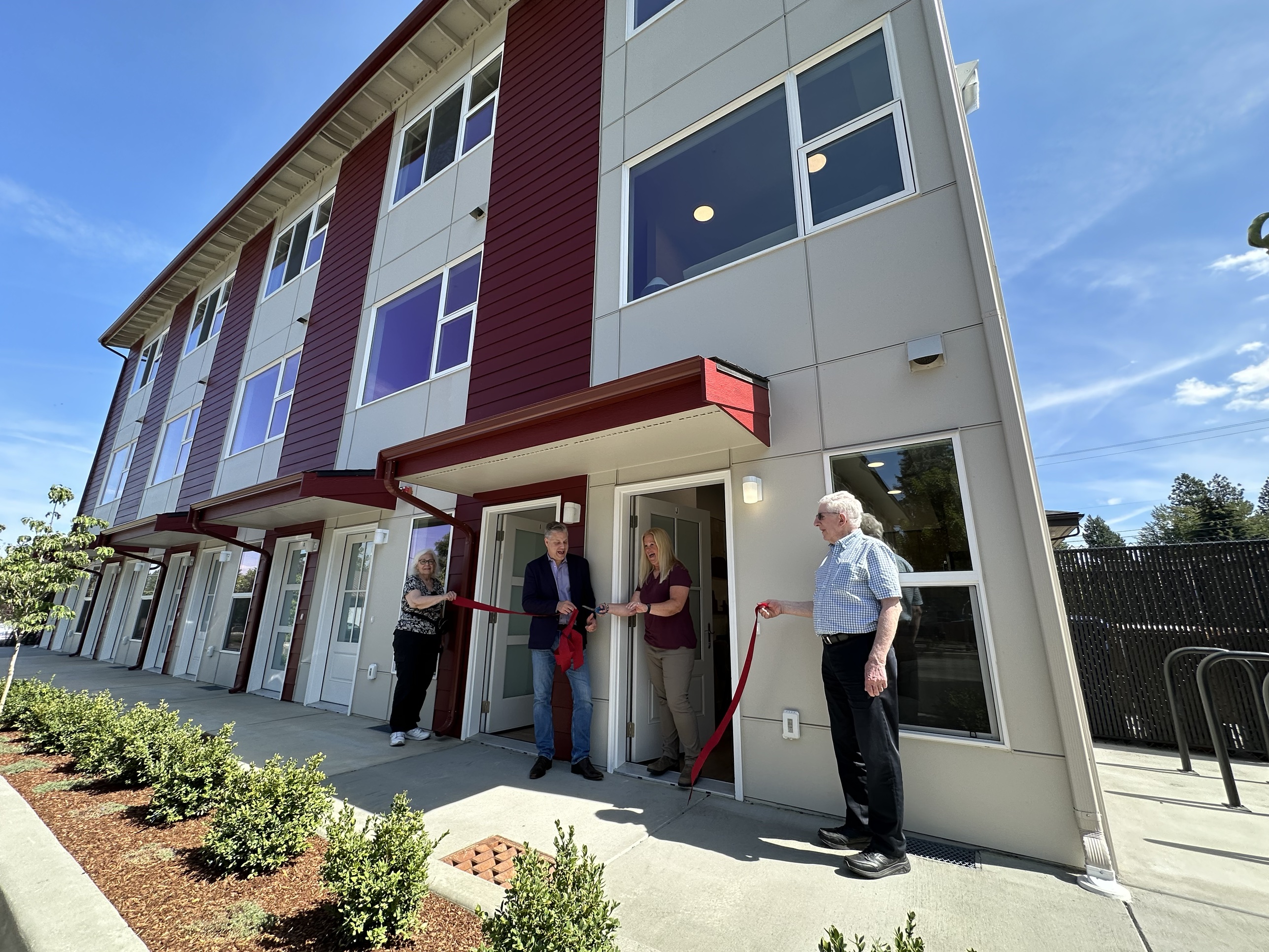 A wide view of the Oldivai Project Zero ribbon-cutting ceremony, with four people holding the ribbon in front of the finished building's open unit doors